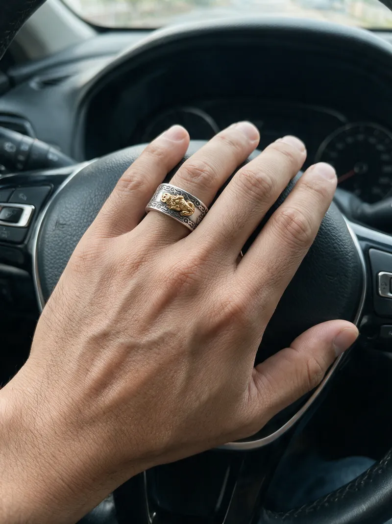 La mano de un hombre en el volante, con el Anillo Pixiu